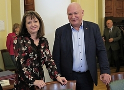Janina Ewa Orzełowska i radny Obermeyer stoją obok siebie. Oboje patrzą przed siebie i się uśmiechają. Ręce opierają o oparcia krzeseł