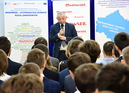 Radny Krzysztof Skolimowski przemawia z mikrofonem do widocznych z tyłu uczniów uczestników spotkania.