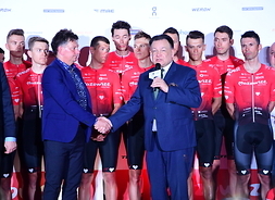 Marszałek Adam Struzik składa gratulacje Dariuszowi Banaszkowi stojąc przodem do uczestników - za nim grupa zawodników w strojach sportowych.