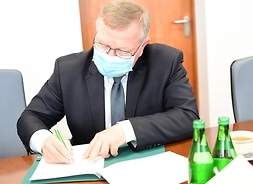 Radny Leszek Przybytniak sieedzi za stołem i prawą ręką podpisuje list intencyjny.