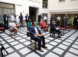 uczestnicy konferecnji prasowej siedzą na jednej z muzealnych sal, z zachowaniem bezpiecznej odległości i w maseczkach