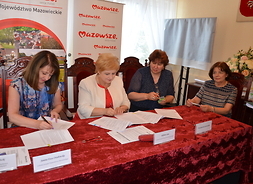 Za stołem  prezydialnym siedzą cztery kobiety i podpisują dokumenty.