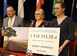 przedstawiciel samorzadu Mazowsze i beneficjenci z gminy Chorzele trzymają w ręku symboliczny czek z wypisaną kwotą dofinansowania z budżetu Mazowsza