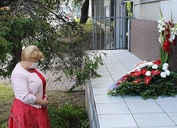 członek zarządu Elżbieta Lanc stoi przed tablicą upamietniającą miejsce masowych egzekucji mieszkańców warszawskiej dzielnicy Wola