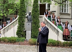 Jacek Boniecki stoi profilem na tle schodów i wejścia do Pałacu Karolin, mówi do mikrofonu.