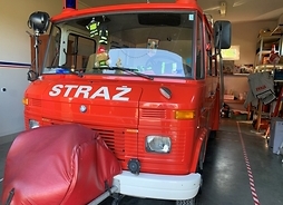 czerwony wóz strażacki z pełnym wyposażeniem stoi przed remizą