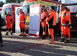 Pięciu ratowników w kombinezonach ratowniczych stoi po obu stronach baneru z logiem Mazowsza