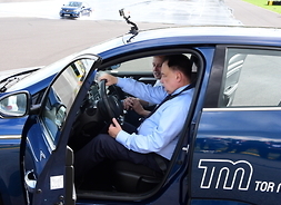 W otwartych drzwiach samochodu treningowego na przednim siedzeniu za kierownicą siedzi marszałek, obok niego siedzi instruktor i udziela instrucji.