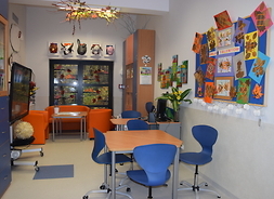 świetlica szkolna, przy ścianie stoi biurko z czterema kszesłami, na ścianach wiszą prace dzieci