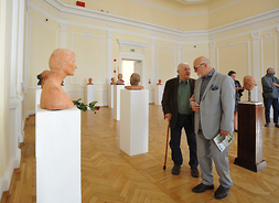 Dwóch uczestników spotkania stoi obok siebie obserwując eksponaty wystawowe.