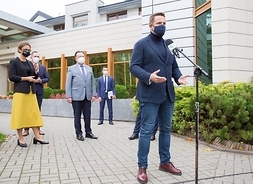 Prezydent Warszawy Rafał Trzaskowski stoi przed mikrofonem. Za nim w Oddali widać marszałka, kobietę i mężczyznę. Wszyscy są w maseczkach.