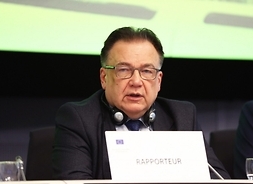 Występujący w debacie siedzi za stołem, na którym na pierwszym planie tabliczka z napisem Rapporteur.