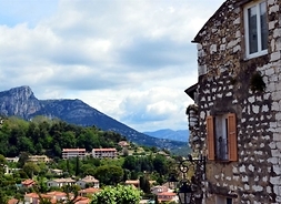 Widok na fragment miasta leżącego u podnóża góry. Z prawej stroy stoi kamienica zbudowana z kamienia.