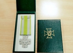 Po lewej medal w ozdobnym rozłożonym etui. Po prawej pudełko z insygniami medalu.