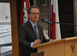 Profesor przemawia podczas konferencji, stoją za pulpitem z logo UW