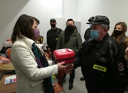 Janina Ewa Orzełowska wręcza strażakowi pudełko z aparatem AED