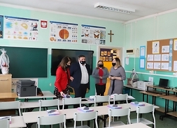 Wnętrze jednej z sal edukacyjnych/ Przy pustych ławkach stoi Janina Ewa Orzełowska oraz dwóch nauczycieli. Wszyscy są w maskach ochronnych