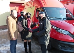 Przy samochodzie dla OSP Dębe Wielkie stoi Janina Ewa Orzełowska i dwaj mężczyźni. Jednemu z nich podaje rękę w geście przywitania się