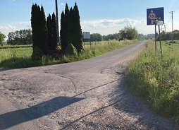 Popękany asfalt na skrzyżowaniu dróg, przy którym stoi przydrożny krzyż