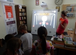 Dzieci wpatrują się w wyświetlany ekran, obok którego stoi nauczycielka