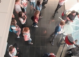 Grupa uczniów sfotografowana z galerii od góry stoi i słucha przewodnika.
