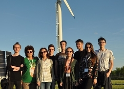 Grupa uczniów stoi przed wiatrakiem służącym do produkcji energii.
