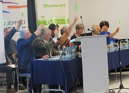 Grupa jurorów siedząca za stołem prezydialnym z tabliczkami ocen w rękach.