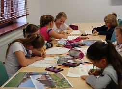 Grupa dzieci siedzi przy stole, wykonują prace konkursowe
