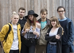Grupa sześciorga studentów stojących na tle drewnianej ściany