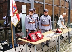 Trzech mężczyzn przebranych w mundury piechoty z 1920 r. za stołem, na którym leżą pamiątki