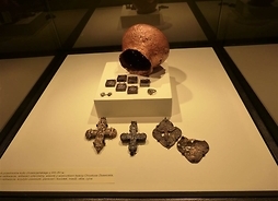 Zniszczony metalowy kociołek a przed nim wyłożone krzyżyki, szkaplerzyki i inne dewocjonalia