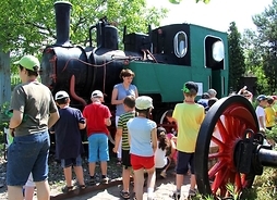 Zabytkowa lokomotywa, a przed nią grupa wycieczkowa, głównie dzieci, z przewodnikiem