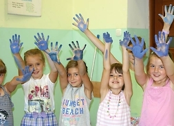 Grupa dzieci z podniesionymi rękami i brudnymi farbą dłońmi