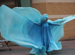 Aktorka ubrana w powłóczystą szatę przedłużoną na rękach jak skrzydła