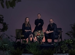 Troje muzyków siedzących na fotelach. Przed nimi bukiet kwiatów w wazonie