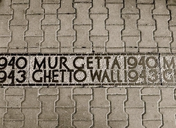 Widok chodnika z brukowej kostki przeciętego granitowym pasem z napisami Mur Getta 1940–1943