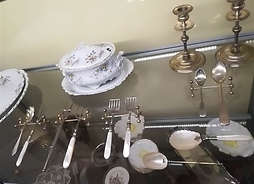 Na szklanej gablocie zestaw wymyślnych łyżeczek i widelczyków ze srebra z perłowymi rączkami na metalowych podstawkach