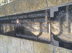 Kamienna ściana z granitową tablicą z dedykacją i widokiem matki boskiej
