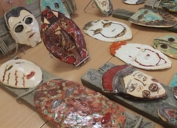 Maski ludzkich twarzy, postaci bajkowych i potworów wykonane z ceramiki leżą na dużym stole