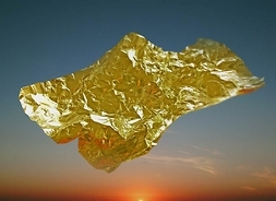 Kawałek złotej folii wznoszący się na wietrze na tle nieba z zachodzącym słońcem