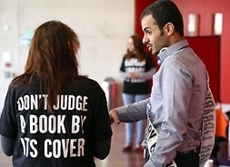 Mężczyzna przepasany szarfą rozmawia ze studentką, która na bluzie ma po angielsku napis „Nie oceniaj książki po okładce”