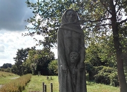 Kamienny pomnik przedstawiający smutną kobietę chroniącą pod fałdami sukni dziecko