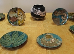 Siedem talerzy i wazon ceramiczny z ozdobami: głównie liście, ale też widok miasteczka oraz smok