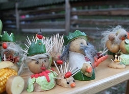 Ludziki zrobione z warzyw, głównie ziemniaków, cukinii, kukurydzy i kapusty oraz wykałaczek stojące na drewnianej ławce