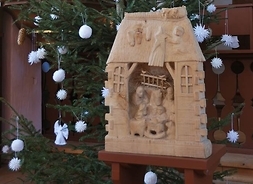 Szopka bożonarodzeniowa rzeźbiona w drewnie, w tle choinka