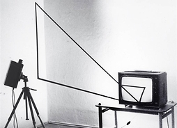 Fotografia kompozycji złożonej m.in. z telewizora na stoliku, kamery i metalowego trójkąta