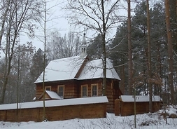 Zdjęcie przedstawia z zewnątrz drewniany kościół w zimowej scenerii