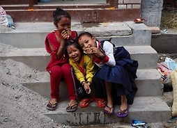 Zdjęcie przedstawia trójkę uśmiechniętych dzieci, siedzących na schodach