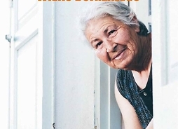 Zdjęcie przedstawia okładkę książki. Starsza, uśmiechnięta kobieta wyglądająca przez otwarte okno