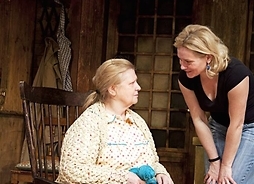 Scena ze spektaklu, przedstawiająca rozmowę dwóch kobiet. Starsza siedzi na krześle młodsza pochyla się nad nią